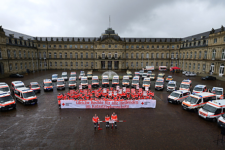 Im Innenhof des Stuttgarter Neuen Schlosses sind DRK-Fahrzeuge im Halbkreis aufgestellt. In der Mitte steht eine Gruppe demonstrierender DRK-Mitarbeiter. Ganz vorne stehen drei DRK-Helfer hinter einer symbolischen Schranke.