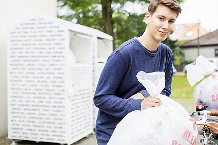 Ein junger Mann läuft mit einem Altkleider-Beutel weg von einem Altkleidercontainer