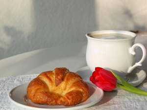 Frühstücksgedeck mit Kaffeetasse und Butterhörnchen auf einem Teller