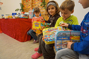 Kinder halten Spielsachen in den Händen, im Hintergrund ein Tisch mit Geschenken