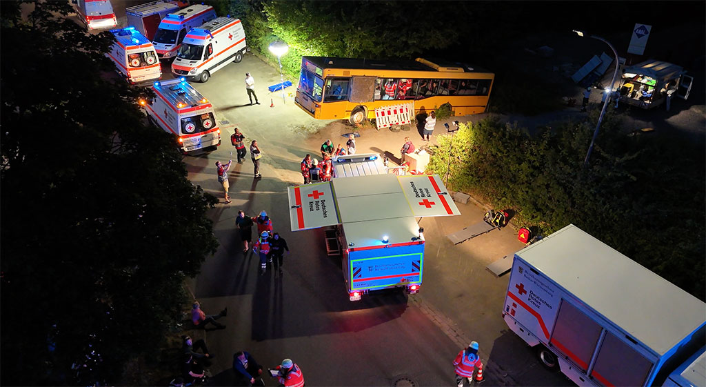Luftaufnahme des verunglückten Linienbusses und mehrerer DRK-Einsatzfahrzeuge bei Nacht