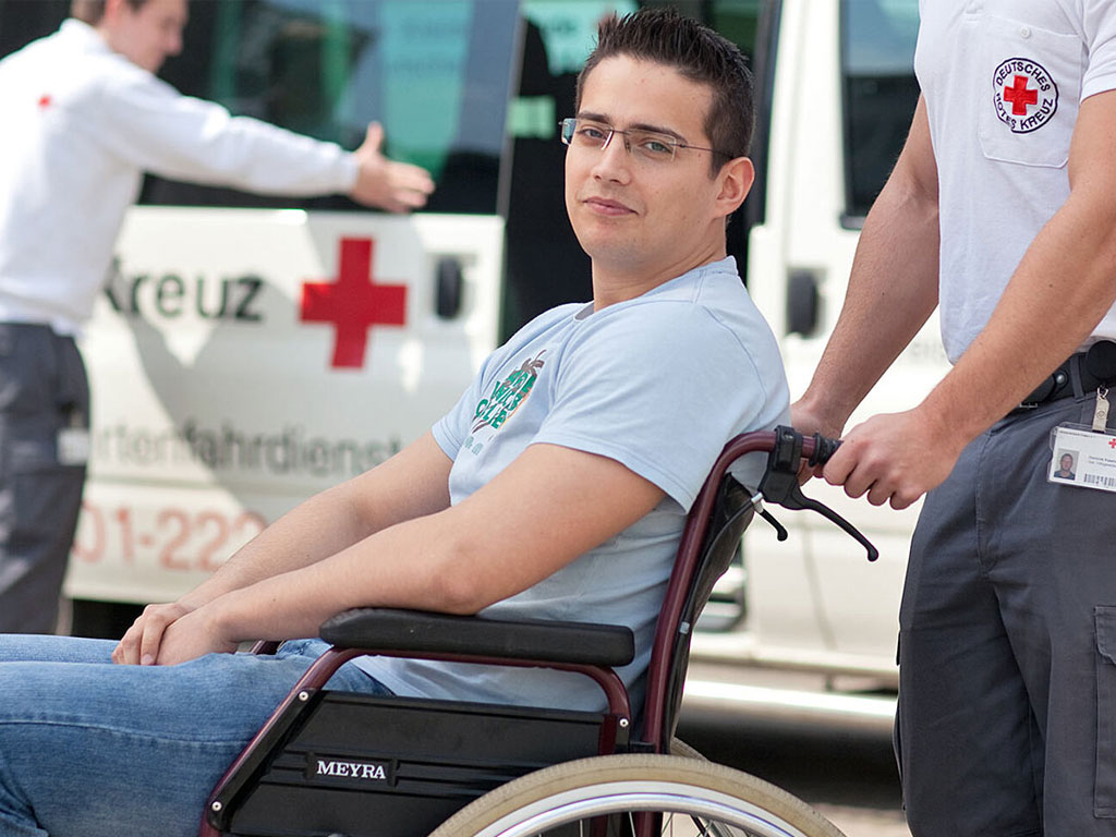 Zwei DRK-Mitarbeiter beim Fahrdienst für einen Rollstuhlfahrer