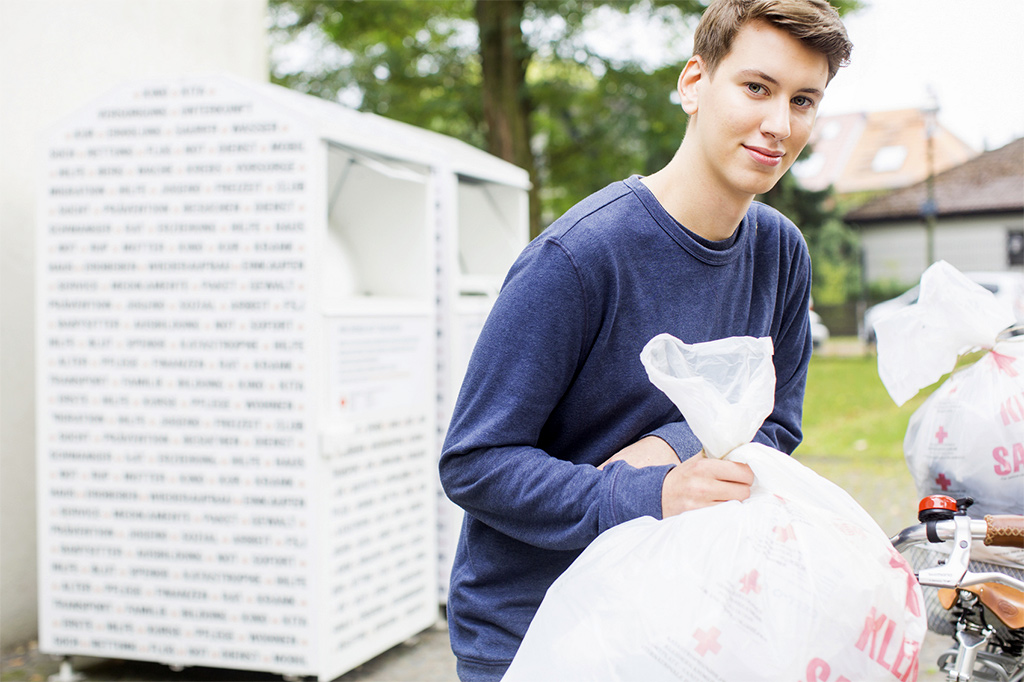 Ein junger Mann läuft mit einem Altkleider-Beutel weg von einem Altkleidercontainer