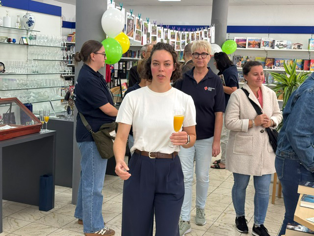 Verschiedene Personen schauen sich im Laden um. Eine Frau hält ein Sektglas gefüllt mit Orangesaft in der Hand.