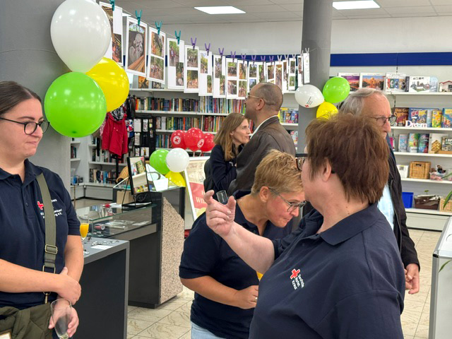 Verschiedene Menschen im Secondhand-Shop, der mit gelben und grünen Luftballons geschmückt ist.