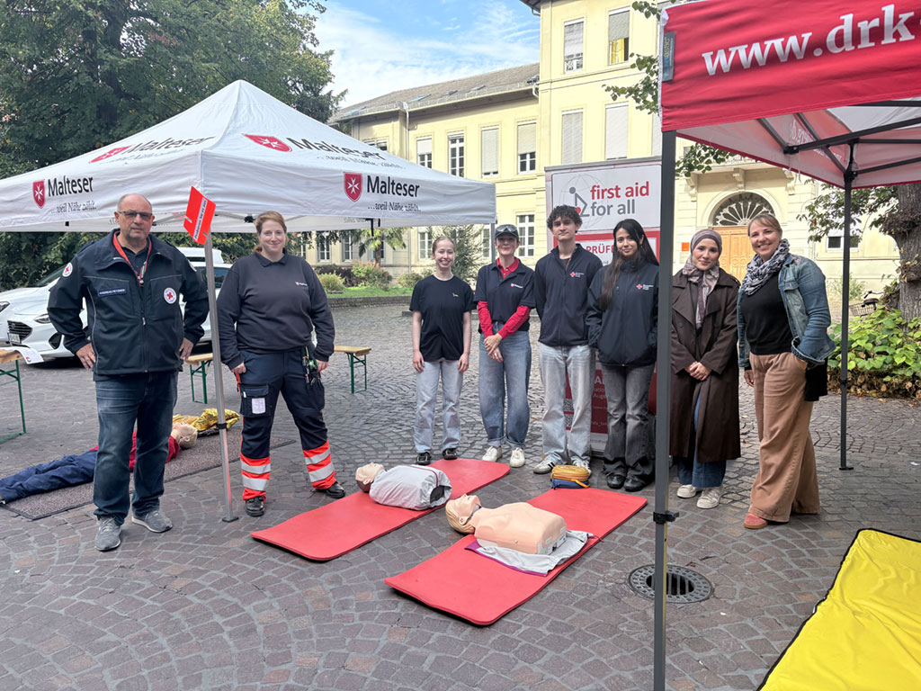 Teams von DRK und Malteser mit einem Stand zum Tag der Wiederbelebung. Vor ihnen liegen Puppen, um erste Hilfe zu üben