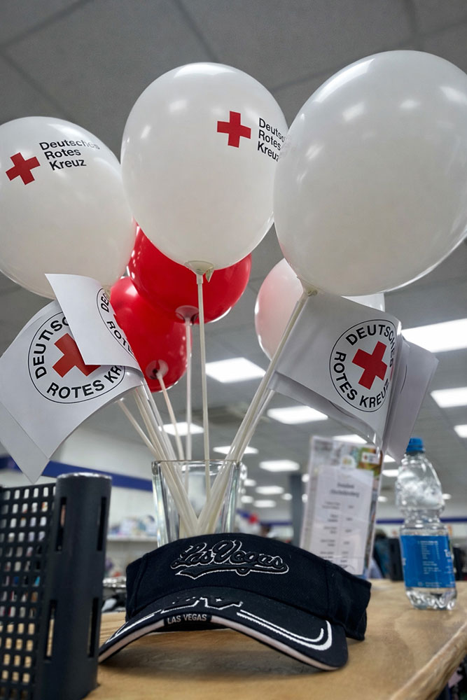 Weiße Luftballons mit DRK-Logo, im Vordergrund eine schwarze Cap mit Schriftzug Las Vegas