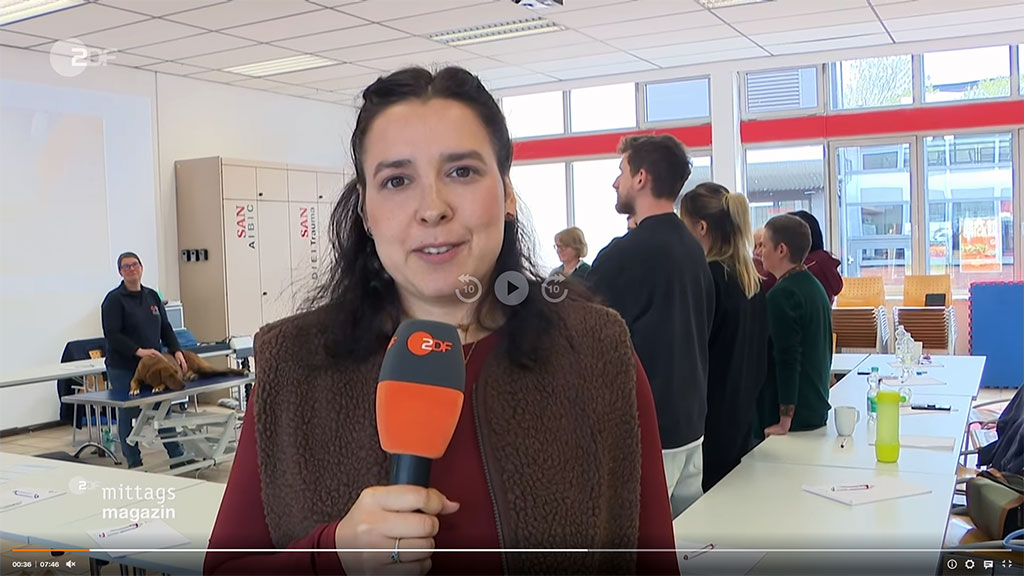 Die TV-Reporterin berichtet mit Mikrofon vom Kurs Erste Hilfe am Hund