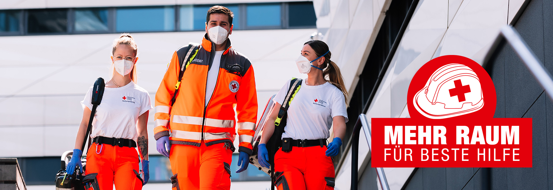 Drei DRK-Mitarbeiter mit ihrer Ausstattung für Erste Hilfe laufen eine Treppe hinunter