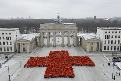 Hunderte rot gekleidete Menschen bilden vor dem Brandenburger Tor ein rotes Kreuz 