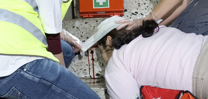 Einer Verletzten wird auf einer Treppe ein Verband am Kopf angelegt