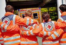 Vier Sanitäter-innen stehen nebeneinander und haben ihre Arme auf den daneben stehenden Kollegen gelegt