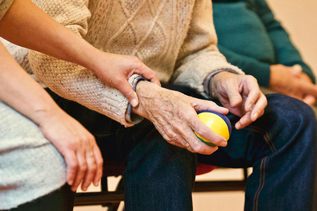 DRK-Mitarbeiterin aktiviert einen Senior mit einem Ball