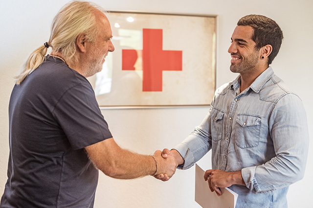 Informationen zu unserem Selbstverständnis Zwei Männer begrüßen sich freundlich