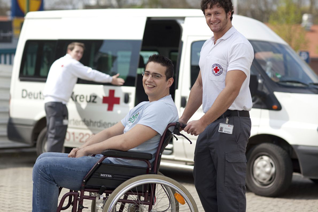 DRK-Mitarbeiter schiebt einen jungen Mann im Rollstuhl